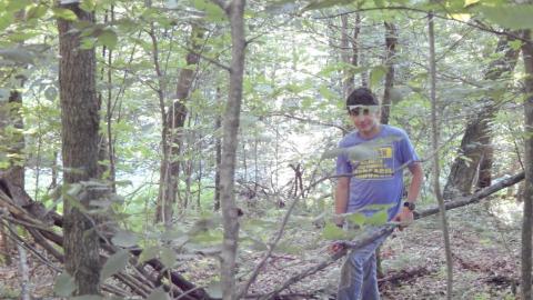 Youth standing among trees in wooded area.