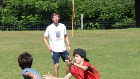 One youth chases another in a game on the field. Counselor looks on from background.