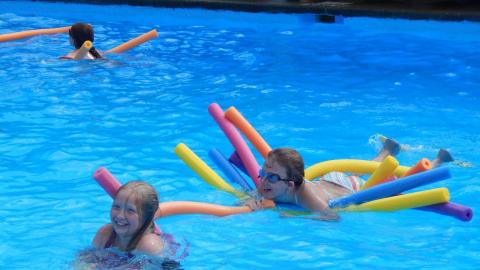 Youth on several pool noodles laughing with friend.
