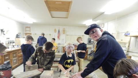 Teen looking into camera as youth around him are in various stages of woodworking projects.