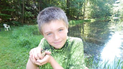 Youth holding a frog near pond.