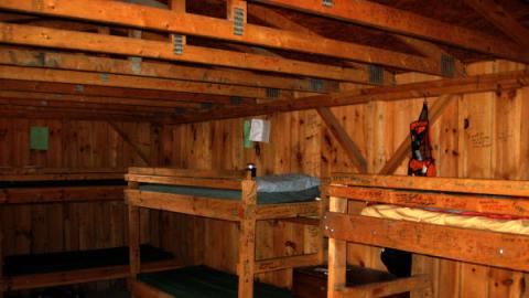 view inside a cabin which shows bunkbeds, a small dresser, and hundreds of signatures on the wooden walls of the cabin.