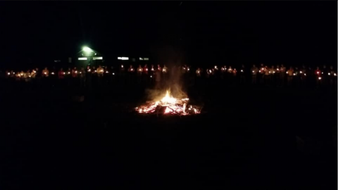campers standing in a circle around a bonfire holding lit candles.