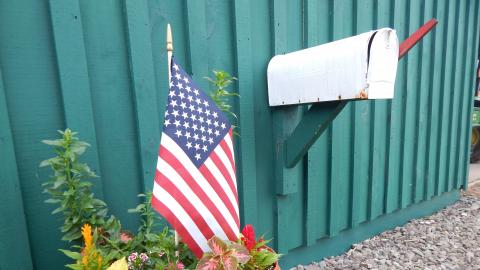 flowerpot with american flag near mailbox on green barn.