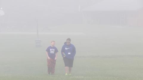 Counselor and youth walk toward the camera from across the field in thick fog.