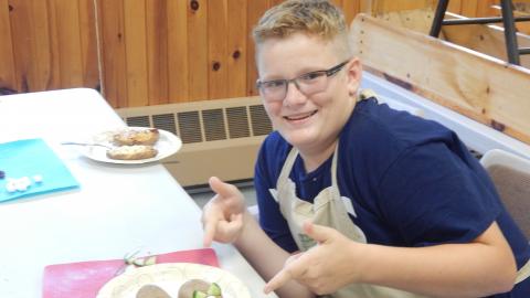Camper smiling and pointing to baked potato mice on table.
