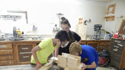 Three youth work together on a wood project.