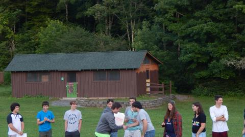 Campers stand in a line with counselors during a skit for the rest of camp seated in front.