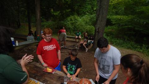 Campers wait in line to add marshmallows to their banana near a fire pit.