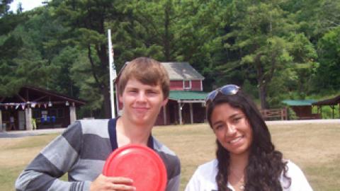 Two teens standing in field. One is holding a Frisbee.