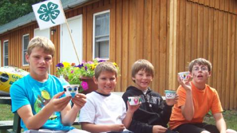 Campers sitting on a bench smiling and holding up a plant project. 