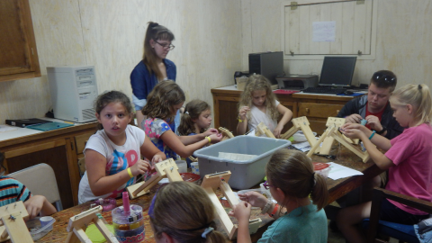 campers gathered around a table stringing beads onto wooden looms.