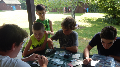 Four youth gathered at a table with one counselor engaged in a game of Magic the Gathering.