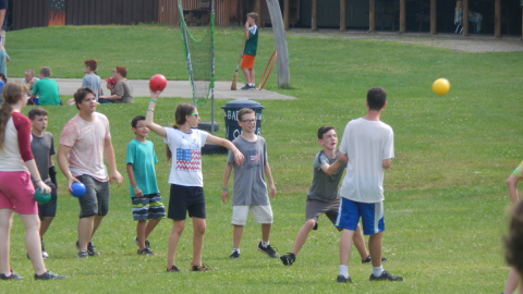 youth throwing foam balls at one station with other groups in the background.