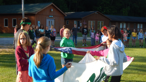 Youth work together to fold the American and 4-H flags while the rest of camp looks on.