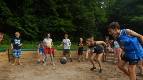 Youth around the edge of the gaga pit while a counselor in the center prepares to hit the ball.