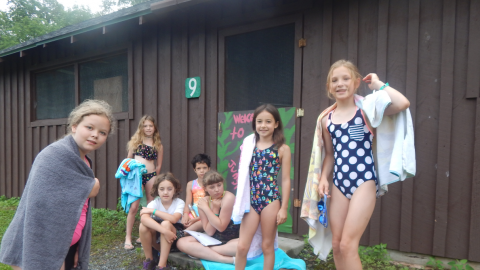 cabinmates sit on stoop of cabin in bathing suits and towels waiting for Polar Bear to be called.