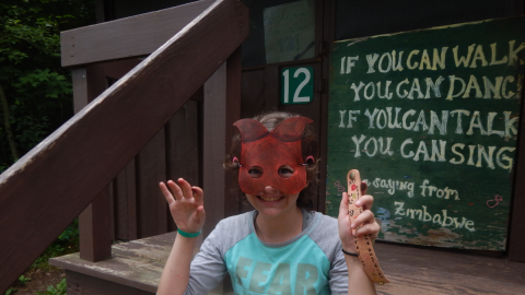 camper seated on cabin 12 porch wearing a mask and holding a crafted bracelet.