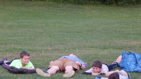 Cabin group laying on sleeping bags in the field laughing.