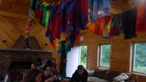 youth working with paracord at a table with colorful tie-dyed bandannas hung over their heads.