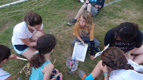 Youth seated in a circle looking at a clipboard and holding markers.