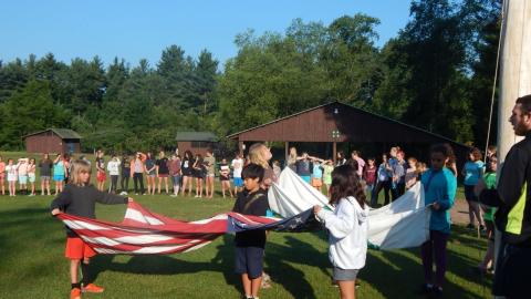Youth work together to fold the American and 4-H flags as the rest of camp looks on.