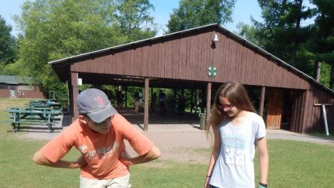 Youth standing on rubber mats. One looks at the other who is bent at the waist holding their hips.