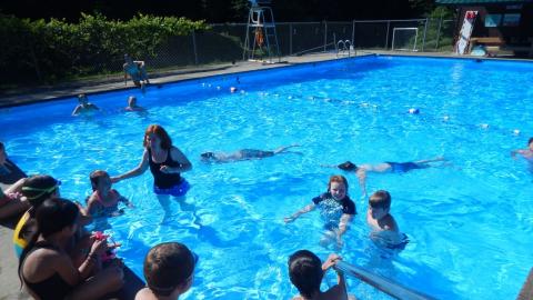Aquatics director in pool with campers as others sit on pool deck.