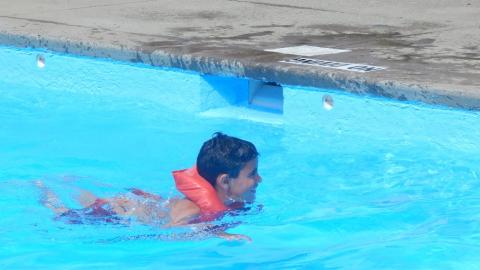 Youth swimming in pool wearing life jacket and smiling.