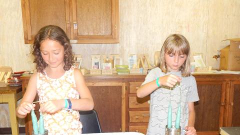 Two youth dipping wick into cans of melted wax forming candlesticks.