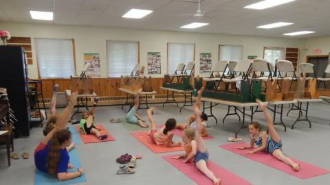 Youth on yoga mats with leg extended toward the ceiling opposite a counselor.