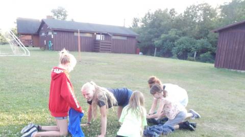 Counselor on hands and knees as campers work around them with blankets.