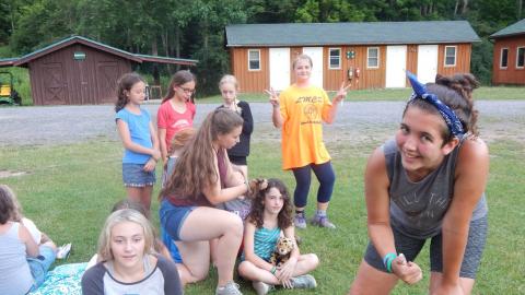 Campers at hair braiding station giving thumbs up or peace signs to the camera.
