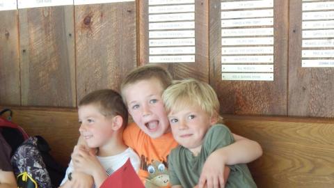 Three youth sitting together on a bench. The middle camper has arms around both campers beside him.