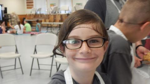 Youth smiling at camera wearing hair net and large glasses.