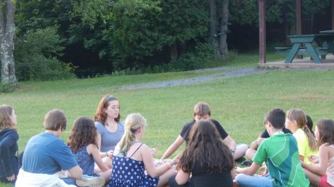 Youth sitting in a circle on the ground with eyes closed.
