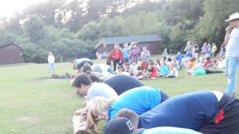 Teams of three roll logs across the field during a game as the rest of camp watches.