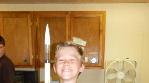 Camper in arm cast smiling and holding up their model rocket.