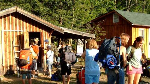 group of youth with hiking bags packed and sleeping bags strapped on getting final supplies together at the backpacking shed before hiking into Lennox forest for a night trip.