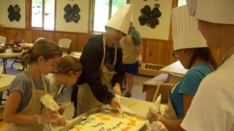 youth decorate a cake with names of campers who had birthdays the month they attended camp.