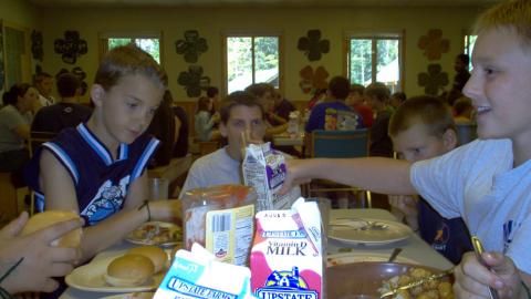 close-up view of campers seated at a table during a meal of burgers and tater tots with cartons of milk.