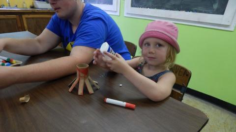 Youth at table holding a bottle of glue with a cut up cardboard tube.