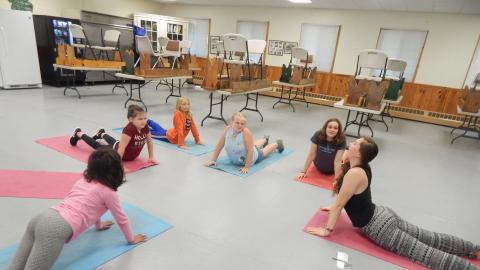 Youth on yoga mats in upward dog position following the lead of a counselor.