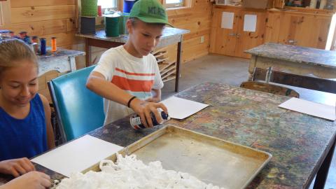 Youth spraying shaving cream into a baking tray in craft hall.