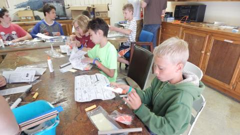 Campers seated together building model rockets from kit reading instructions.
