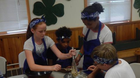 Four youth in aprons work together to whisk batter they have mixed.
