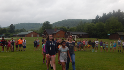 color guard approaches the flag pole in the middle of a large circle of campers.
