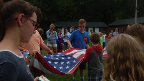 Campers work together to fold the 4-H and American flags while the rest of camp looks on.
