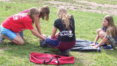 four youth work together to roll up a tent.