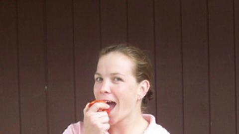 adult volunteer bites into an apple while smiling at the camera.
